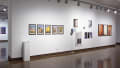 Photograph of a long wall with grouped photographic work by three different artists. On the far left is a glimpse into another room with a single framed print visible.
