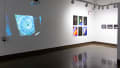On the left is a wall projection of a clock, to its right are six abstract photos on panels. Three small black-framed night landscape photos are visible on the far right.