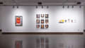 Image of gallery wall with a solarized photograph in metal frame, with red print inset and overlaid, on the far left. In the center is a three-by-three grid of portraits, and on the far right is a group of collages and appropriation-based artworks.