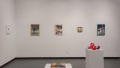 Multiple views of SVA Gramercy Gallery. There are paintings, photographs, mixed media and textile artworks hung on the walls. There are ceramic sculptures, books and 3D prints on pedestals throughout the gallery and lobby. 