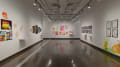 Multiple views of SVA Chelsea Gallery. There are illustrations, monitors, and paintings hung on the walls. Shelves have posters, books, CDs and artist take-aways.