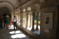 In the arched hall, artworks hang on either side as visitors stand and observe. The closest work looks to be a print made with organic shapes.