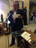 A man in a suit stands at a microphone as he addresses a crowd.