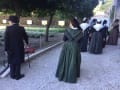 People enter the exhibition in traditional garb and costumes. Women are wearing long dresses and shawls around their shoulders, while a man dressed in all black carries a cane.