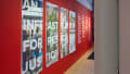 Exhibition view of An Infrastructure for Restorative Justice, featuring hallway painted red with a large posters and text on the wall.