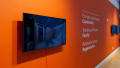 Installation image of an angled view of an orange wall with text and three monitors.