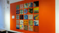 Installation image of an angled view of an orange wall with carpet squares of differing patterns.