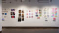 A  wall shows seven more projects containing prints and books. Some of the projects do not have books displayed beneath them, and some projects contain original paintings or drawings.