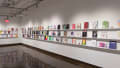 Colorful books are displayed in three rows on long shelves that span the width of gallery four.