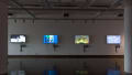 Installation image showing four monitors of equal size along a large wall, playing animated reels.