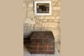 A framed painting of a brown trunk hangs from a stone wall above a real-life brown trunk.