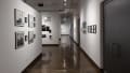 Installation image showing 12 framed photos on the left wall a long hallway to the front gallery.