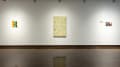 Exhibition installation image featuring 3 artworks: small abstracted wall installation, muted yellow painting, and two small silk prints.