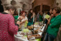 Several art exhibit viewers around a buffet table while chatting.
