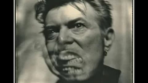 A black-and-white image of a man grimacing. He is in motion so the face is triple imposed and blurred.