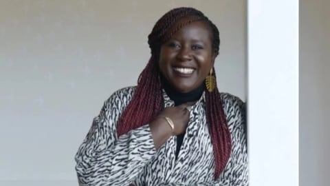 A photo of Fatima Bintou Rassoul SY leaning against a white pillar. She is in a black and white patterned dress with her hand under her chin. 