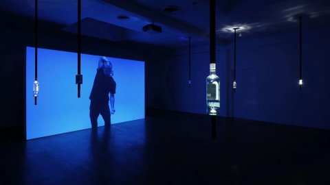 Image of projected video with man dancing and bottles of vodka hanging from the ceiling.