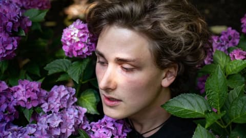 A photo of a young adult inside of a hydrangea bush with their head above the flowers 