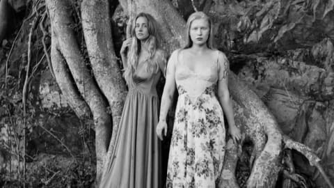 Black and white photograph of the two artists standing barefoot in front of a large tree root.