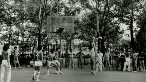 Sepia-tone B&W landscape shot image of Asian men playing basketball outside.
