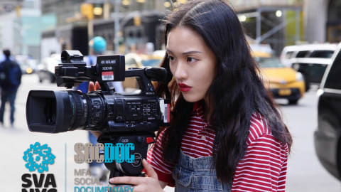 A girl looks intently into a video camera, filming something out of sight, on a city street