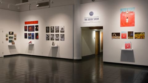 Photograph of lobby gallery space with "The Book Show" vinyl lettering over hallway, with illustrations on walls to either side.