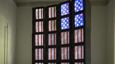 Twenty-four screens, stacked in four columns, displaying one large stylized American flag when viewed at a distance.