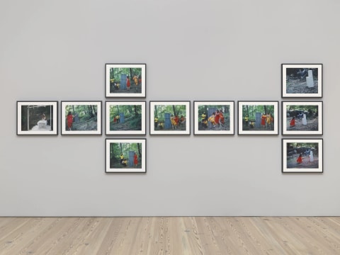 An installation view of 11 prints documenting a performance done by a group of people in a forest