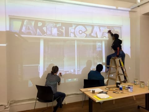 Three people painting a projected image on a wall.
