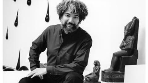 Black and white photpgraph with artist sitting in front of art.