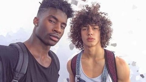 Two young men of color taking a selfie with the sky behind them.