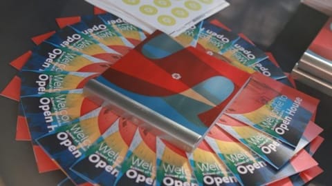 A compact disk lies atop an array of colorful open house brochures. Brochures organized in in a circle.