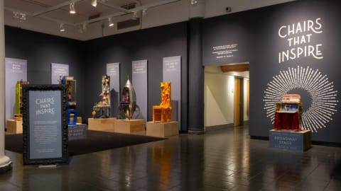 Photograph of exhibition "Chairs That Inspire" featuring chairs made around a single theme or from one type of object. Installed in lobby gallery space.