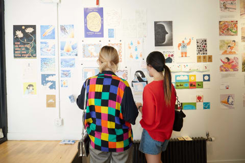 Two people looking at a wall of illustrations