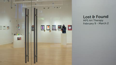 Photograph from outside gallery space with artworks visible through glass doors and the text "Lost & Found" on the wall to the right.