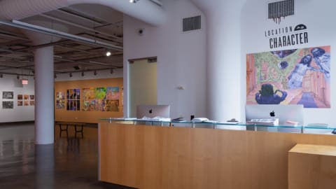 View of exhibition from entrance to gallery with "Location As Character" name placed above reception desk to the right.