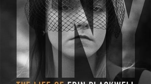 Caucasian woman wearing netting over her face, staring blankly forward. Greyscale, except for three words which are in orange.