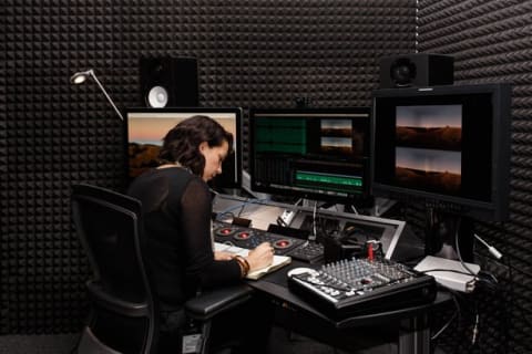 Woman taking notes at a desk set up for audio editing in a soundproof room.