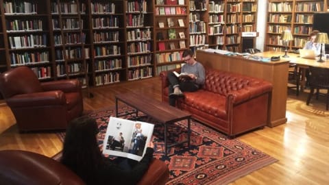 Three people reading or working in a room filled with books.