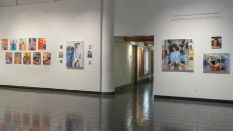 Photograph of main entryway of gallery with paintings on either side of a hallway, with exhibition title above paintings on the right.
