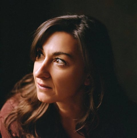 A color portrait photo of a woman, photographer Lynsey Addario, pearing out of the darkness into the light 