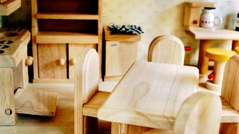 Photo of a wooden kitchen in a doll house, including table and four chairs, an oven, a cabinet and some other background furniture