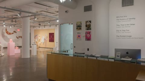 An art gallery featuring several art installations in the back ground. Additionally, there is a desk and an iMac in the foreground.
