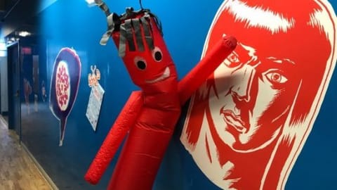 Large images on a blue wall with a red blow up character leaning into the wall.