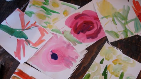 Flower paintings and drawings scattered across a desk by Peter Hristoff's students.