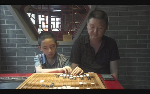 A man watches as a little boy plays Go.