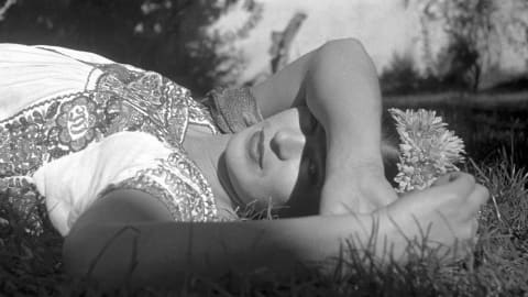 a B&W photograph of artist Frida Khalo, lying down, her arm draped across her eyes