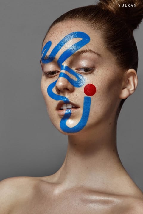 A photograph of a woman with yellow and blue paint on her face shot by Ruo Bing Li for Vulkan Magazine.