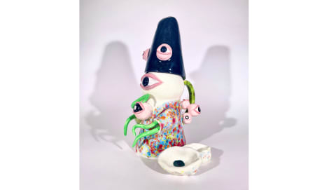 Yinyao Liang, Mad Eyes, 2023, ceramic, 11.5" X 5.5" X 7.5", 1" X 2.75" X 1.75" - Ceramic art with eyes on the body, a blue hat, green tentacles, and a floral shirt. Beside it lays two tiny circular dishes.