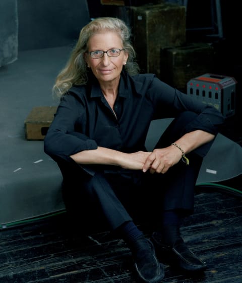 Color photograph on Annie Leibovitz sitting on the floor of a photographic studio looking into the camera. 